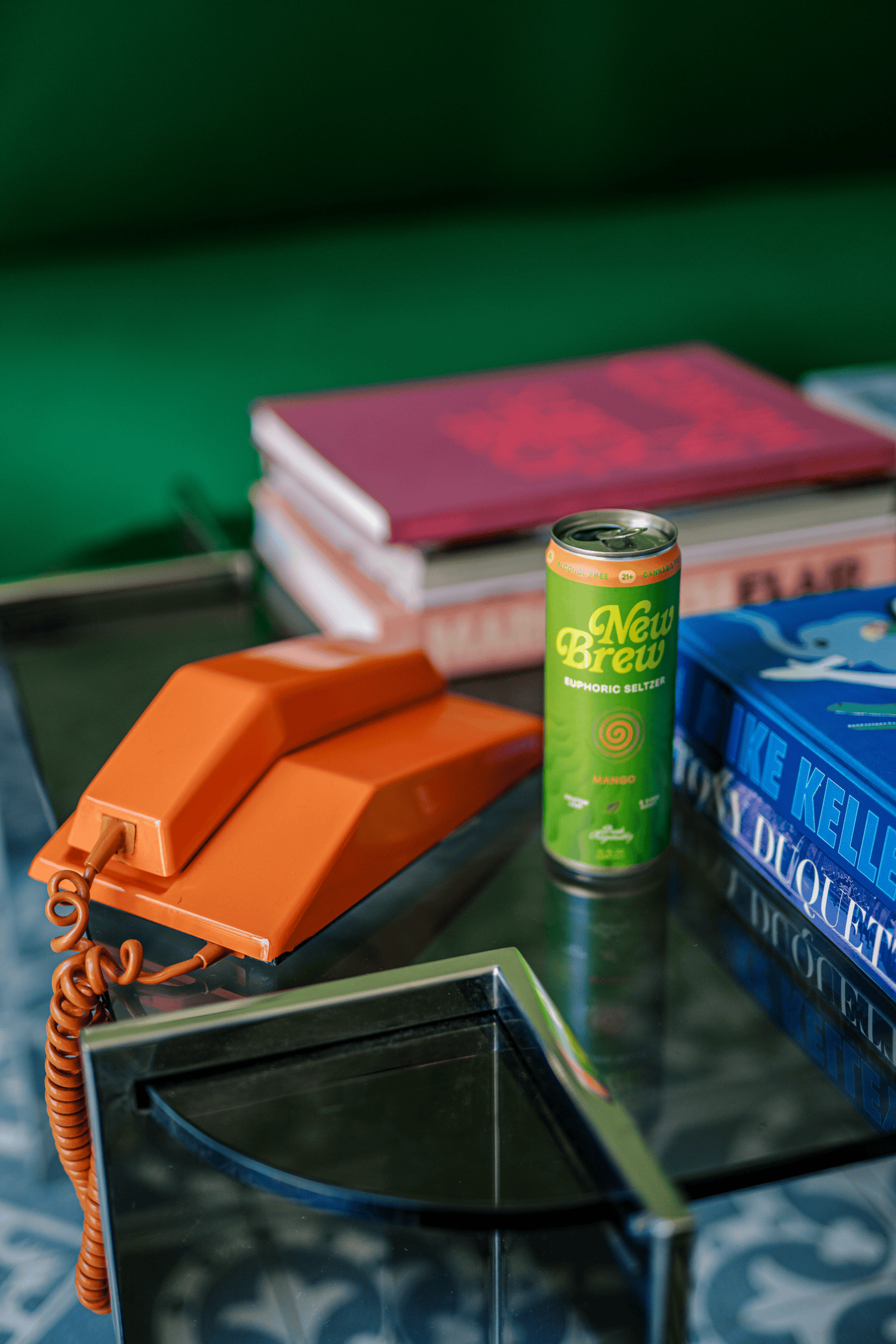 Full-color product still life of a canned beverage styled with a vintage radio and orange telephone on patterned tile