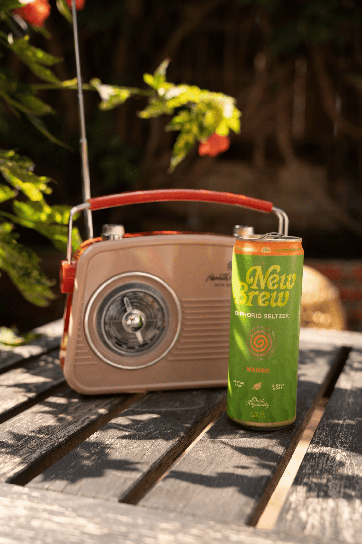 Full-color product photograph of a canned beverage beside a retro portable radio on a wooden outdoor table