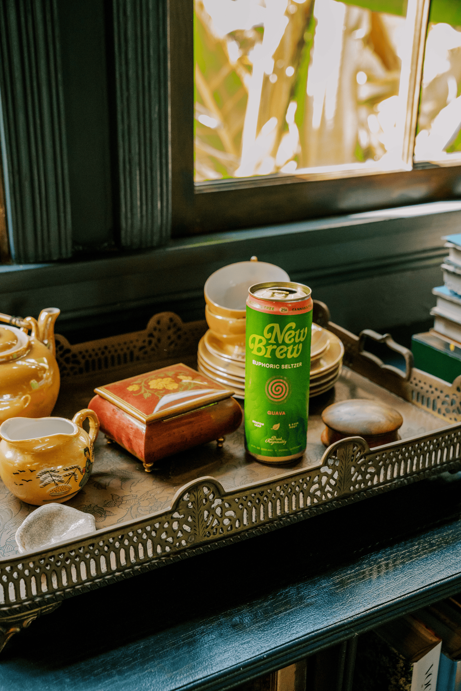 Full-color product still life of a canned beverage styled among vintage books and decorative objects on an ornate tray