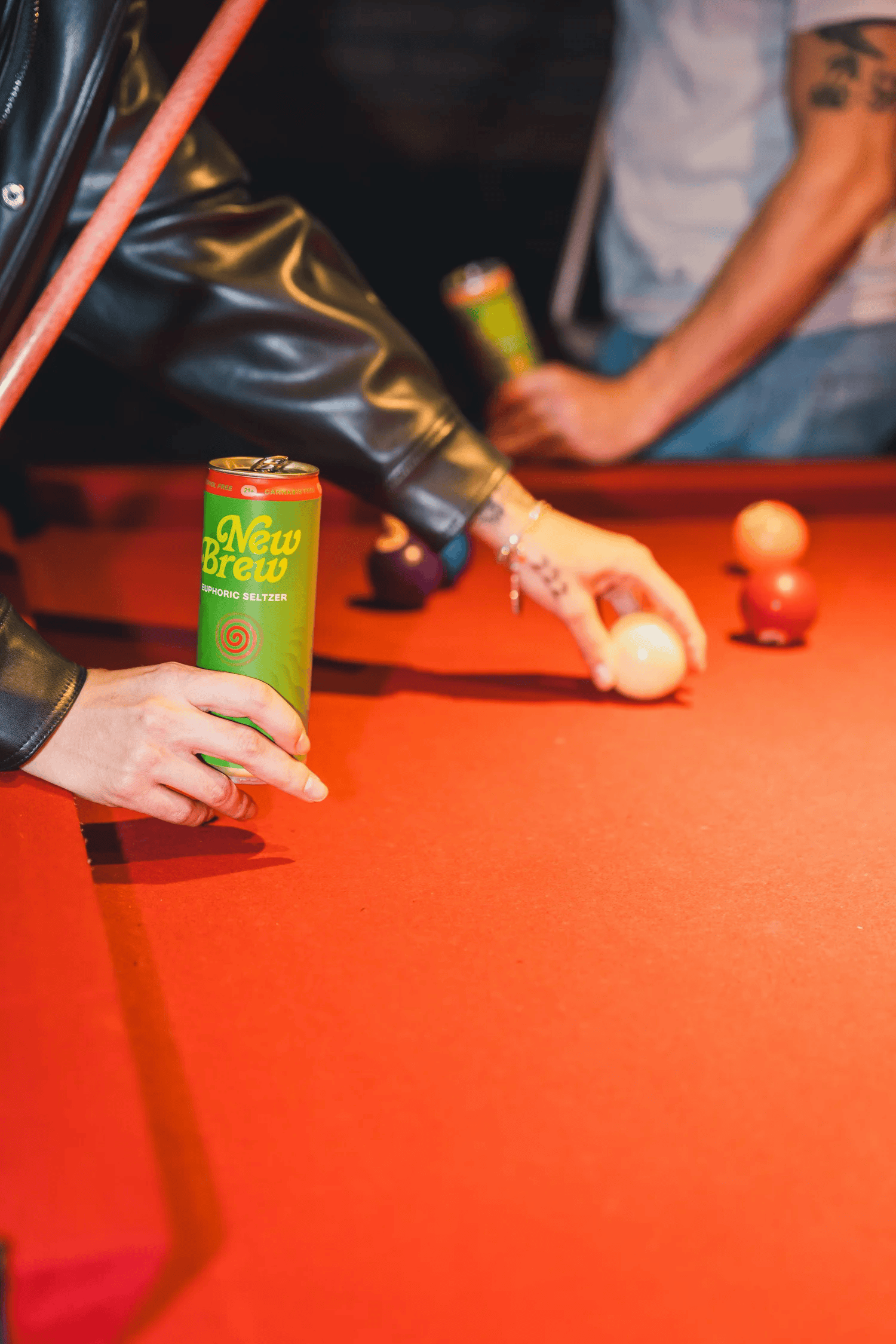 Full-color lifestyle campaign photograph of a canned beverage held over a pool table during a game