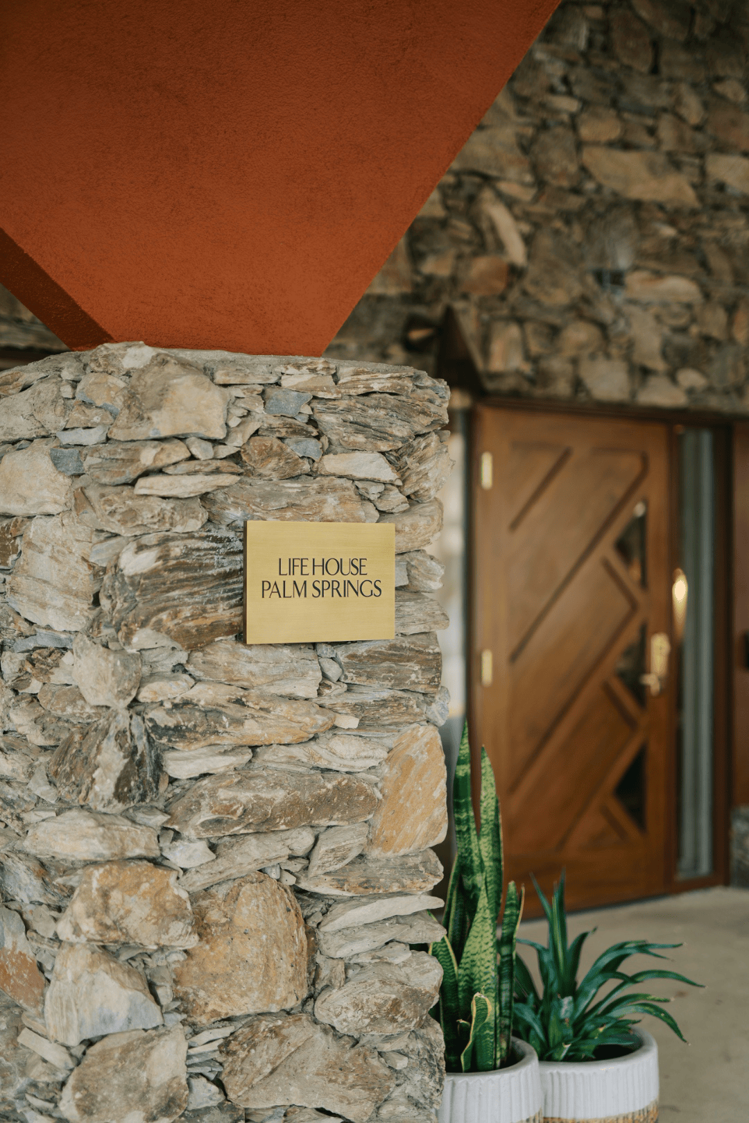 Brass entrance signage mounted on a stone wall beside a wood-paneled front door, full-color architectural photograph