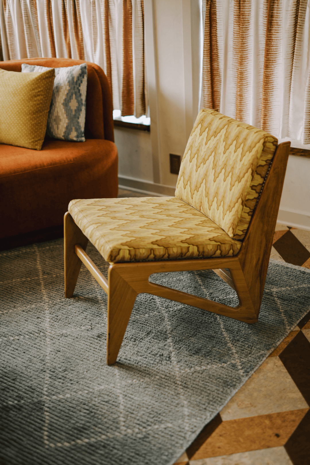 Mid-century chevron-upholstered lounge chair with angular wood legs on a patterned area rug, full-color interior photograph
