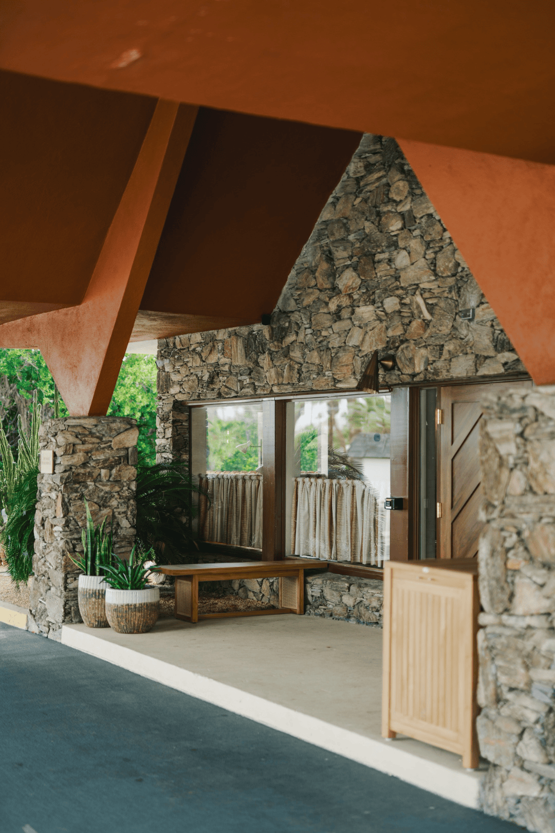 Covered entrance walkway with terracotta ceiling beams, stone columns, and potted plants leading to the front door, full-color architectural photograph
