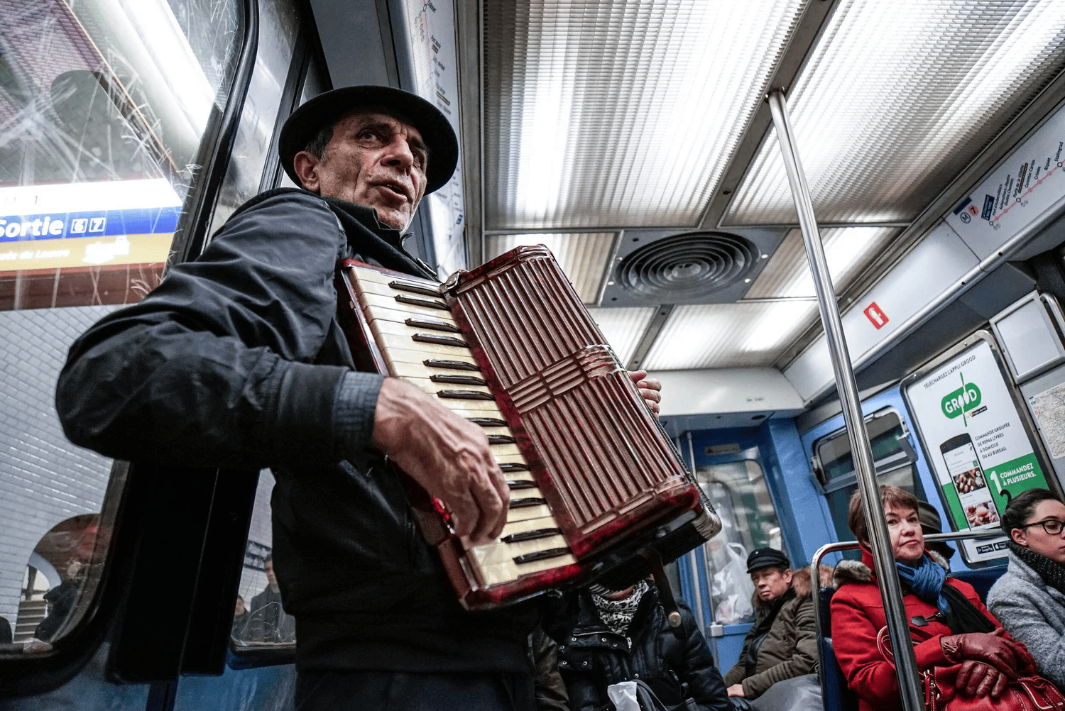 Full-color candid portrait of a street musician playing accordion on a Paris metro train