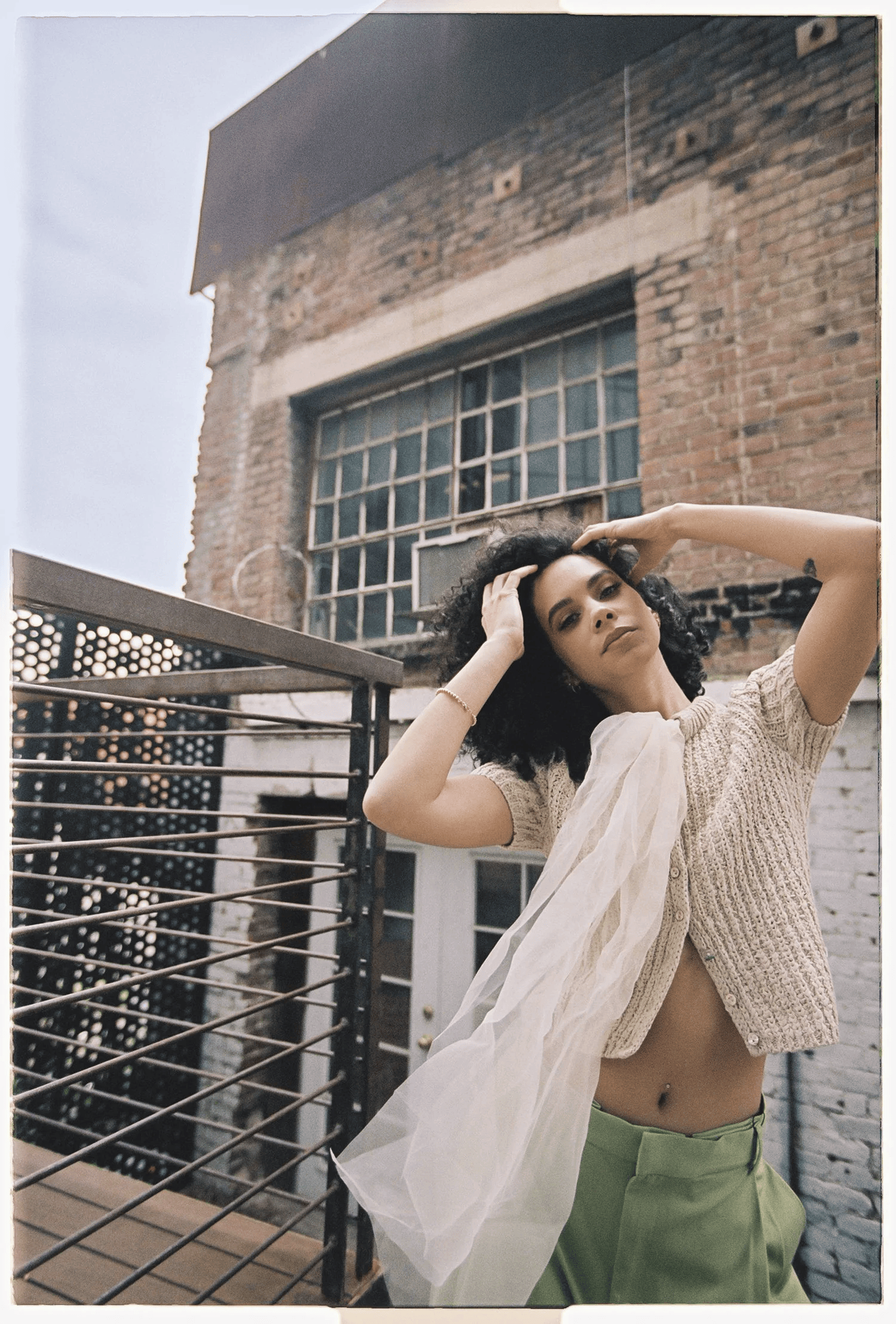 Full-color film-toned portrait of a woman on a rooftop terrace against exposed brick and industrial windows