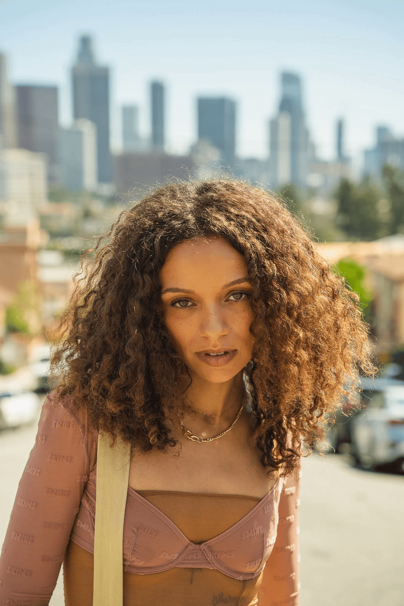 Full-color portrait of a woman with curly hair against a blurred downtown Los Angeles skyline