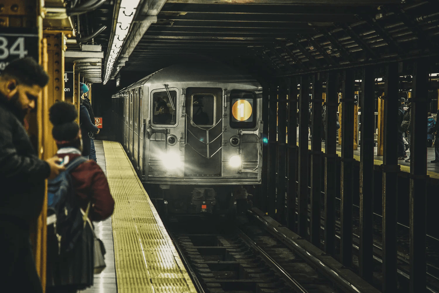 Full-color documentary photograph of a subway train arriving at a New York City station platform
