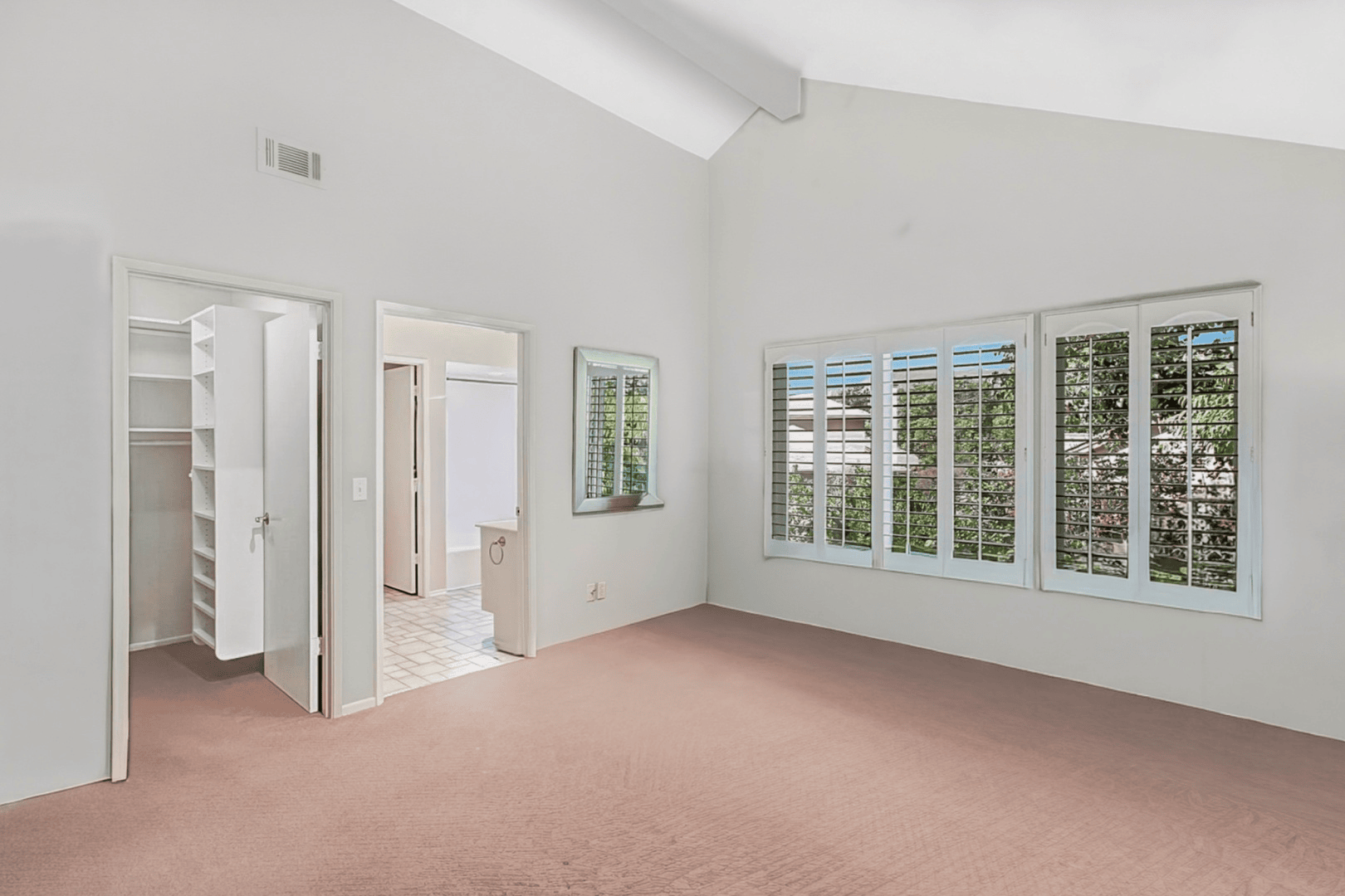 Full-color interior photograph of a vacant primary bedroom with vaulted ceiling and soft natural light