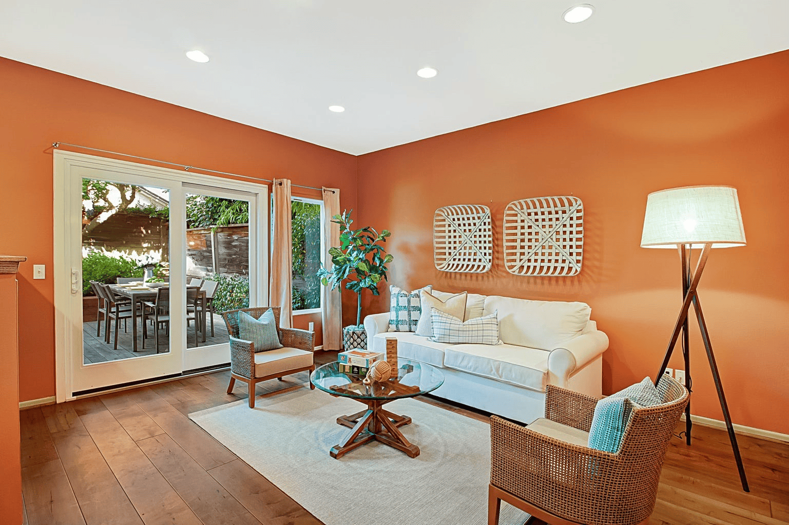 Sun-lit living room staged with white sofa and rattan accent chairs, sliding glass doors open to a wood deck, full-color interior photograph