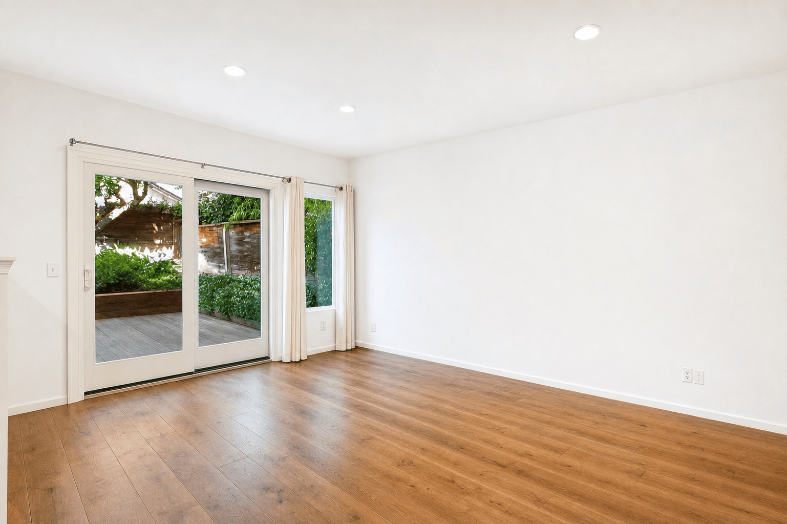 Vacant living room repainted white with sliding glass doors to a wood deck, full-color interior photograph