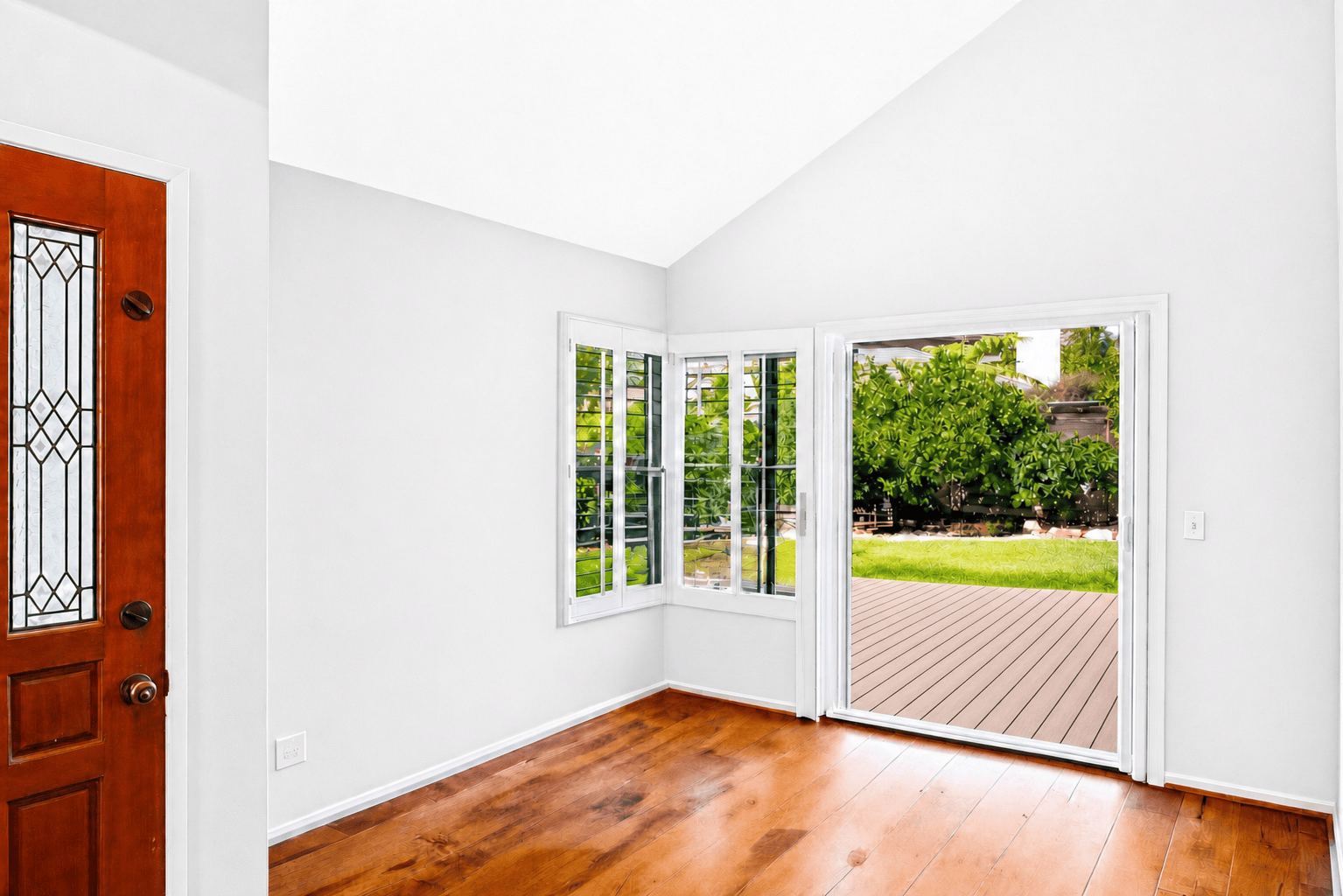 Sunroom entry repainted white with stained glass front door and view to the backyard deck, full-color interior photograph