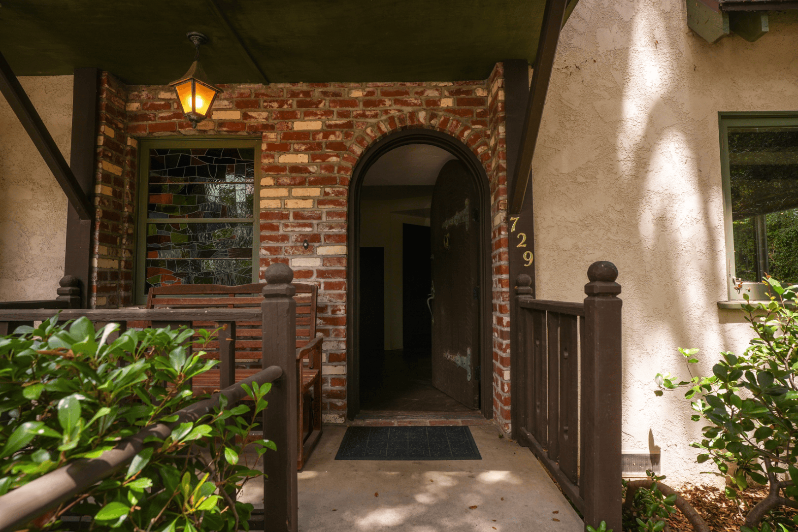 Arched brick entryway with stained glass window and covered porch bench, full-color architectural photograph