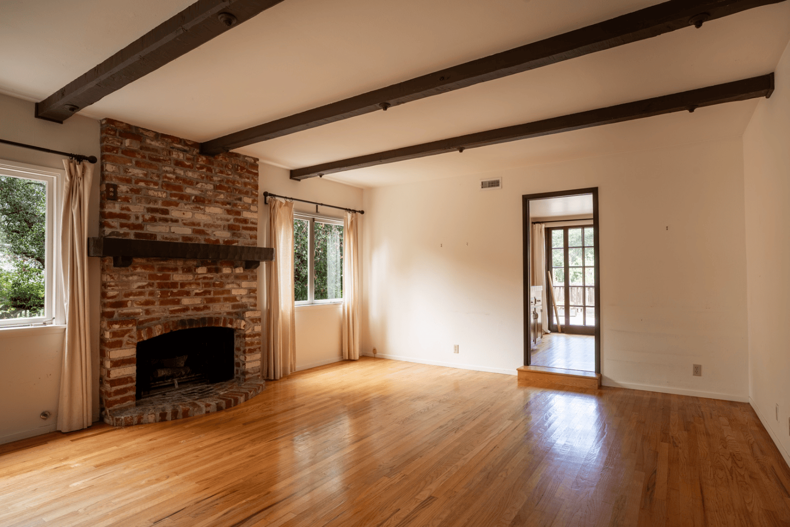 Vacant living room with exposed wood ceiling beams and brick fireplace, full-color interior photograph