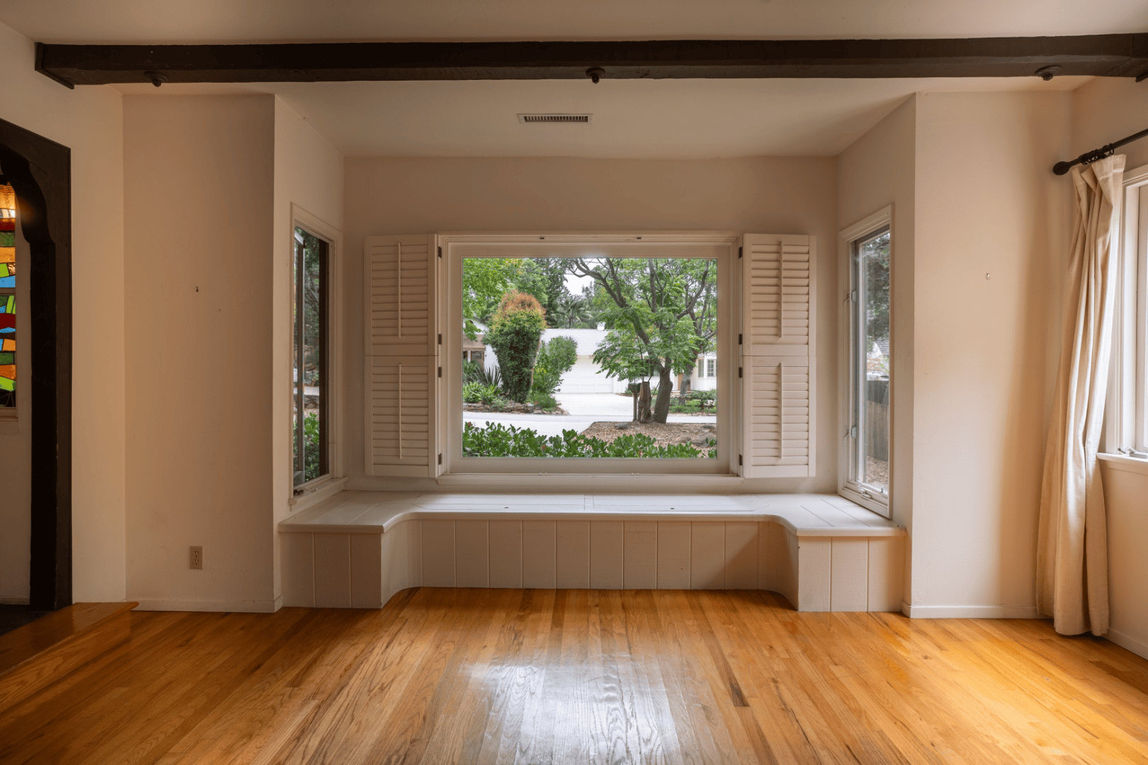 Built-in bay window seat with shuttered windows overlooking the front garden, full-color interior photograph