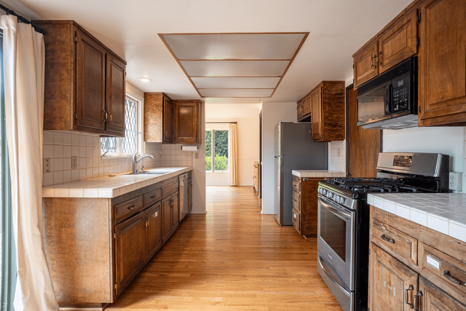 Galley kitchen with wood cabinetry and tile counters opening to the dining area, full-color interior photograph