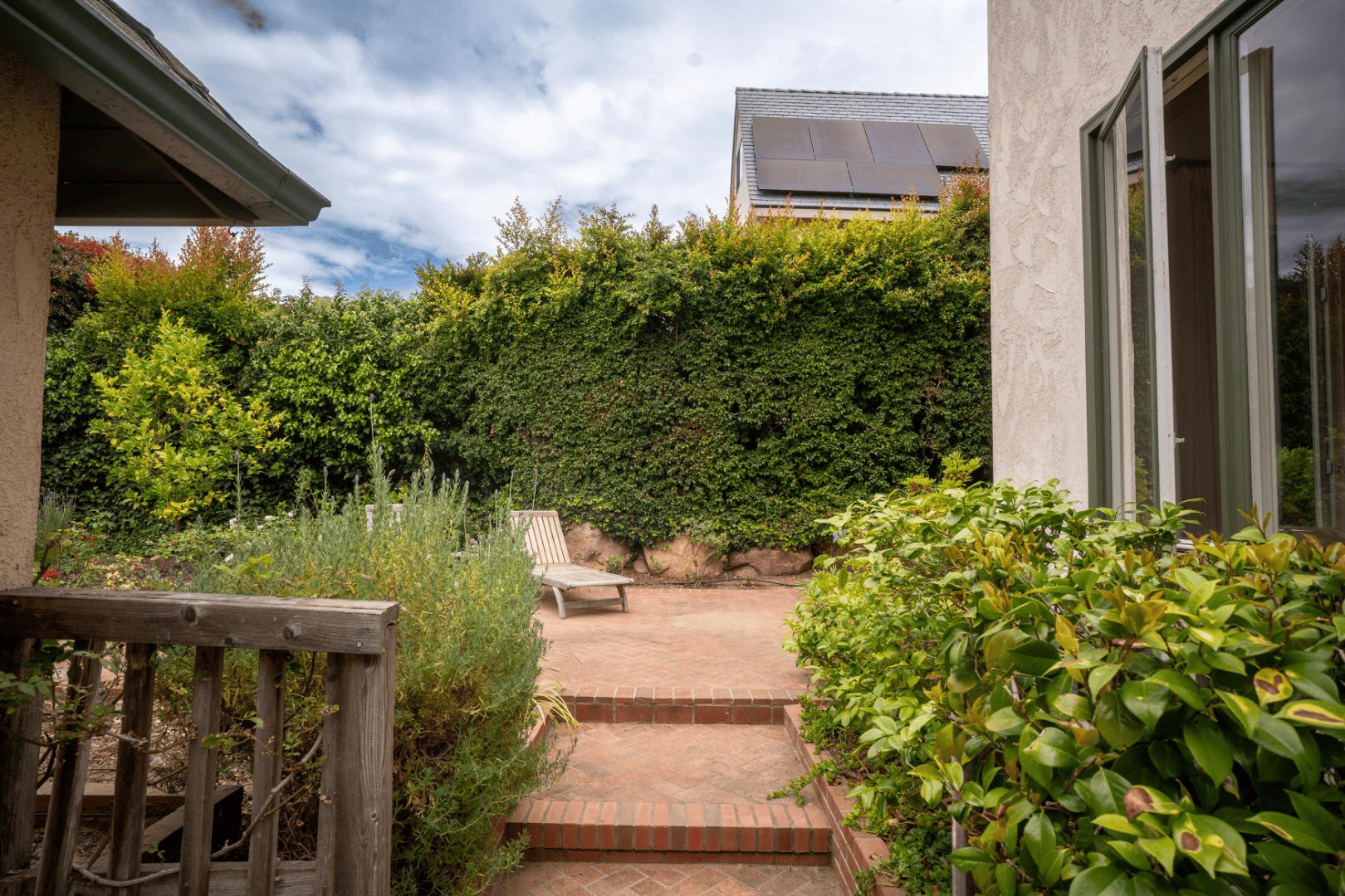 Brick garden path leading to a private patio with lounge chair and mountain views, full-color exterior photograph