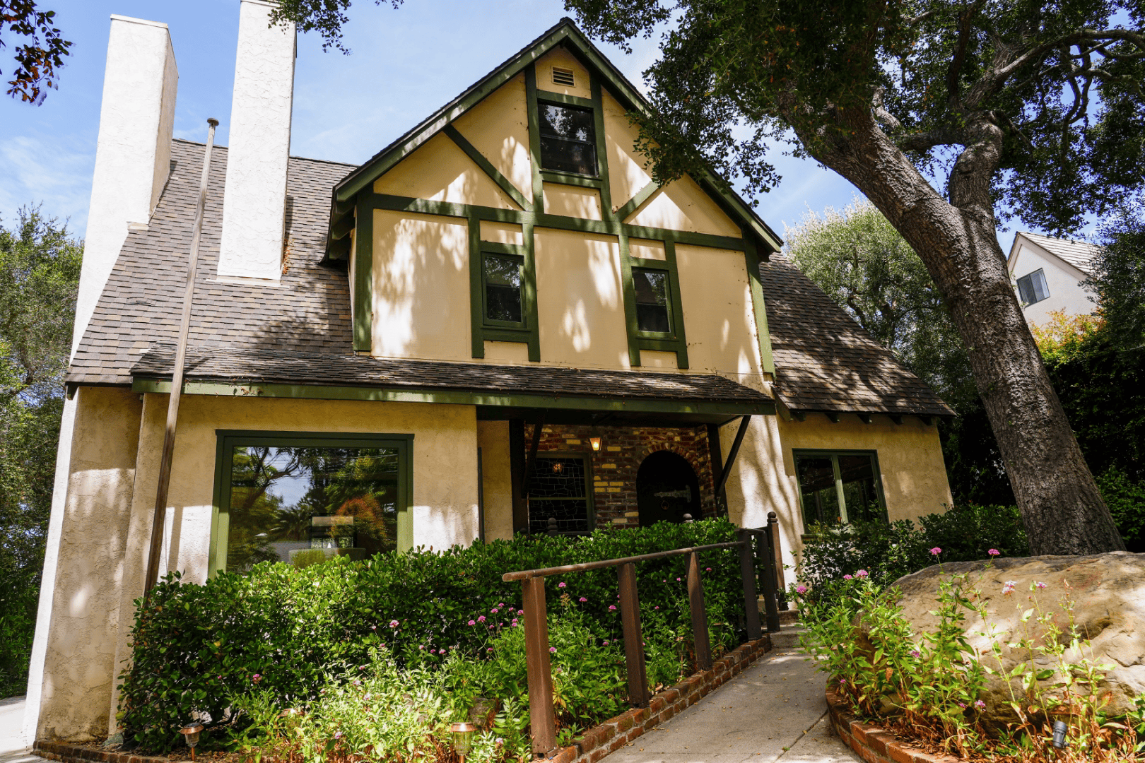 Wide angle of the Tudor-style home's front gable and half-timbered upper story through the tree canopy, full-color architectural photograph