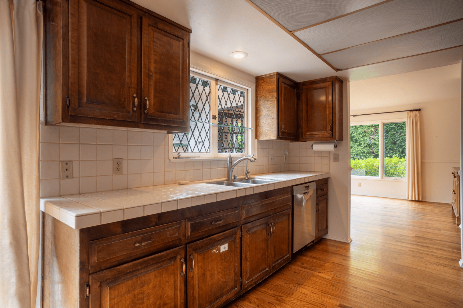Kitchen sink and dishwasher beneath a leaded glass window with view to the backyard, full-color interior photograph