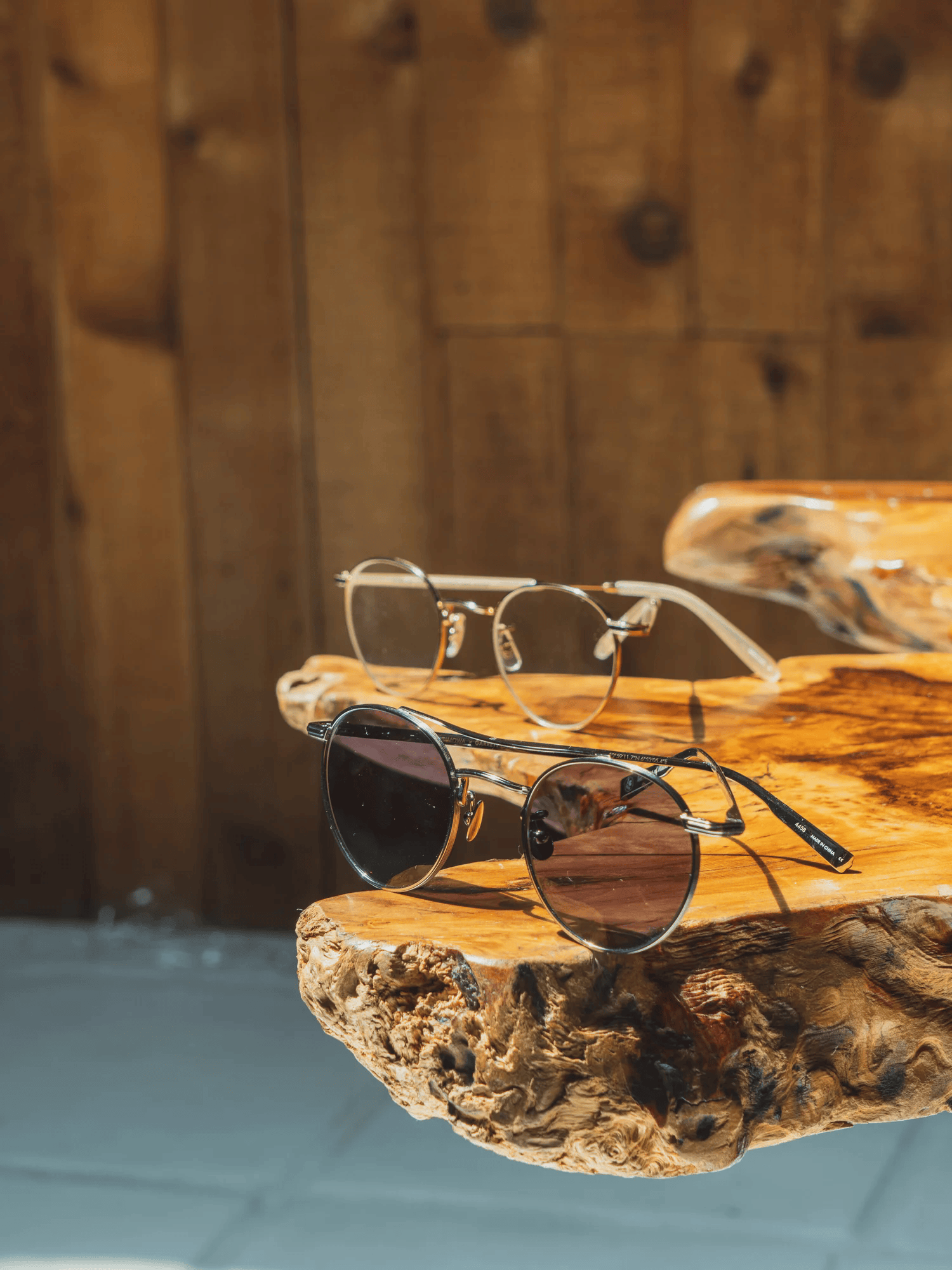 Full-color still life photograph of two pairs of vintage sunglasses and eyeglasses on a live-edge wood slab