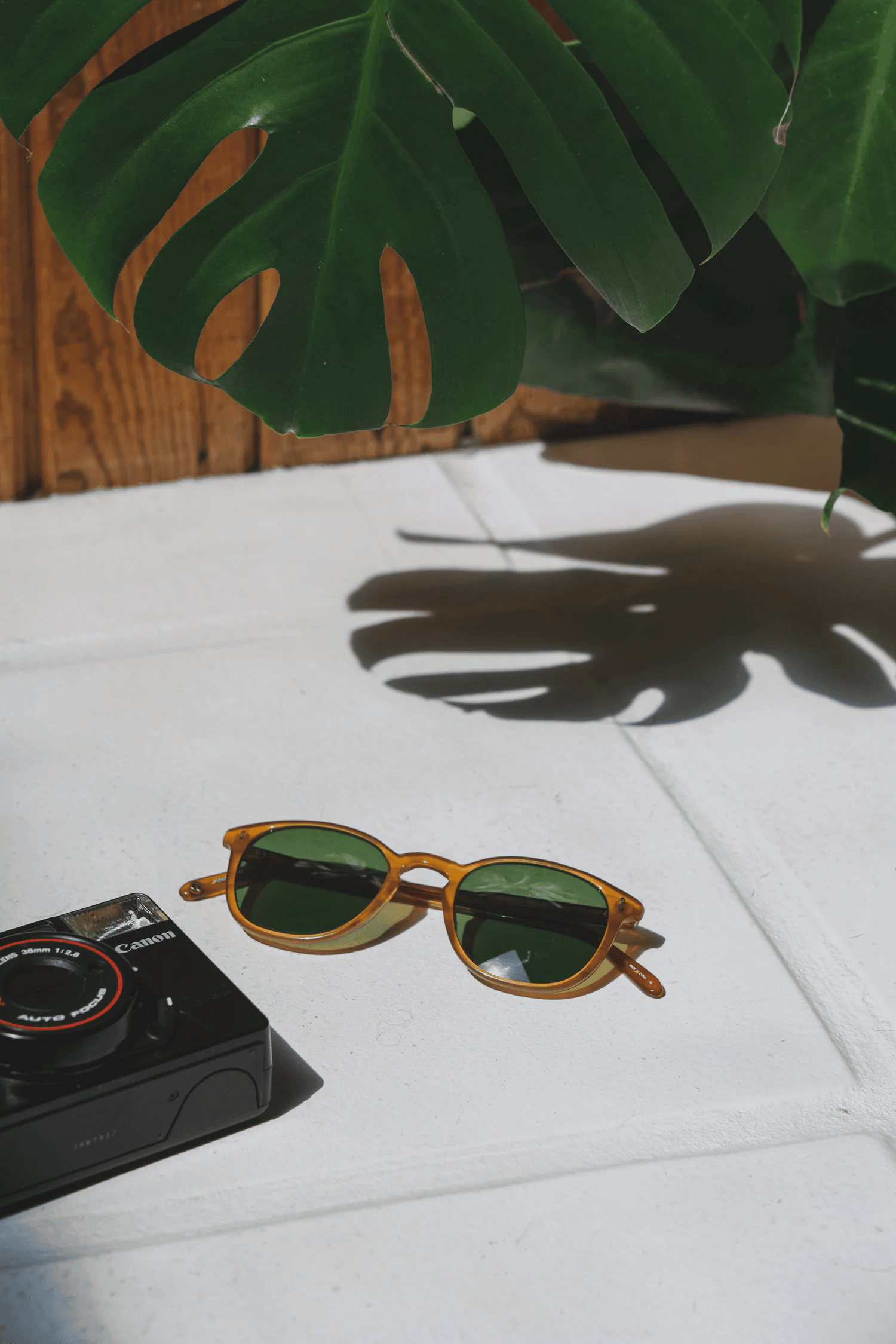 Full-color still life photograph of round wire-rim sunglasses paired with amber acetate frames on white tile